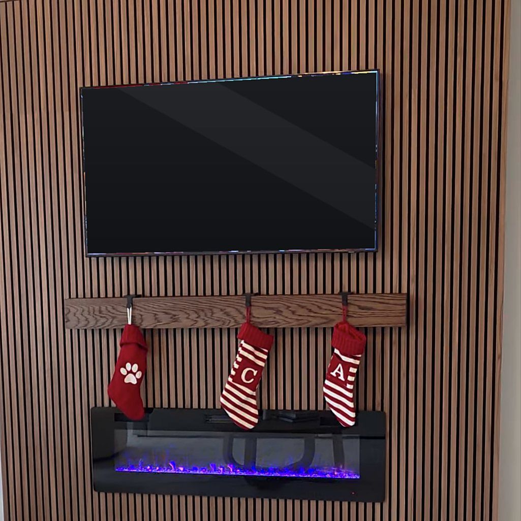 Floor-to-ceiling wood slat accent wall with a mounted TV, oak mantel shelf, and wall fireplace